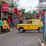 Vibrant street scene in Kolkata featuring classic yellow Ambassador taxis amidst lively urban ambiance.