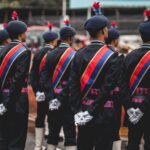 Formal military parade featuring soldiers in traditional uniforms with sashes and berets.