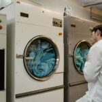 A man wearing a white shirt uses industrial washing machines in a public launderette.