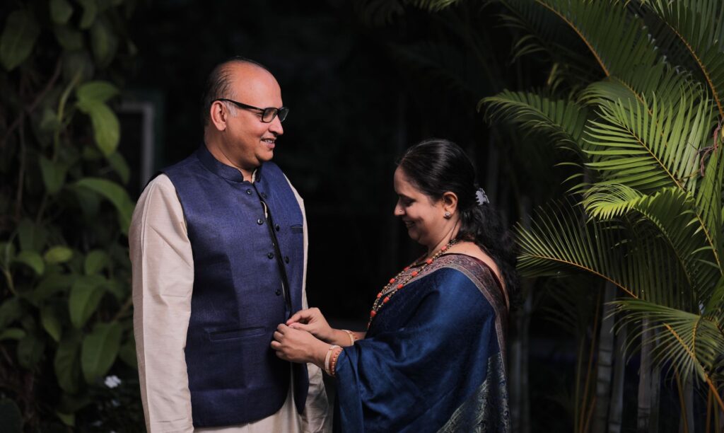 An Indian couple in traditional clothes smiling together in a lush outdoor setting.