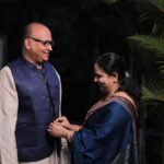 An Indian couple in traditional clothes smiling together in a lush outdoor setting.