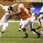 Athletes in action during an American football game on a grassy field.