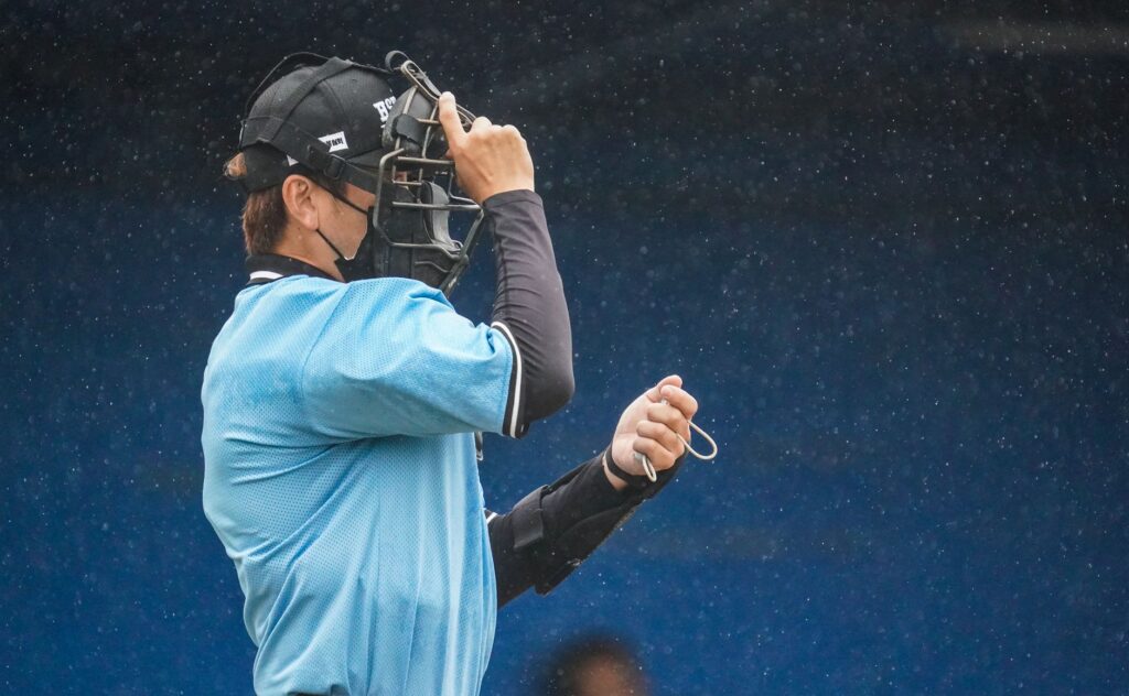 A baseball umpire adjusts his mask during a rainy sports event, capturing focus and dedication.