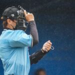 A baseball umpire adjusts his mask during a rainy sports event, capturing focus and dedication.