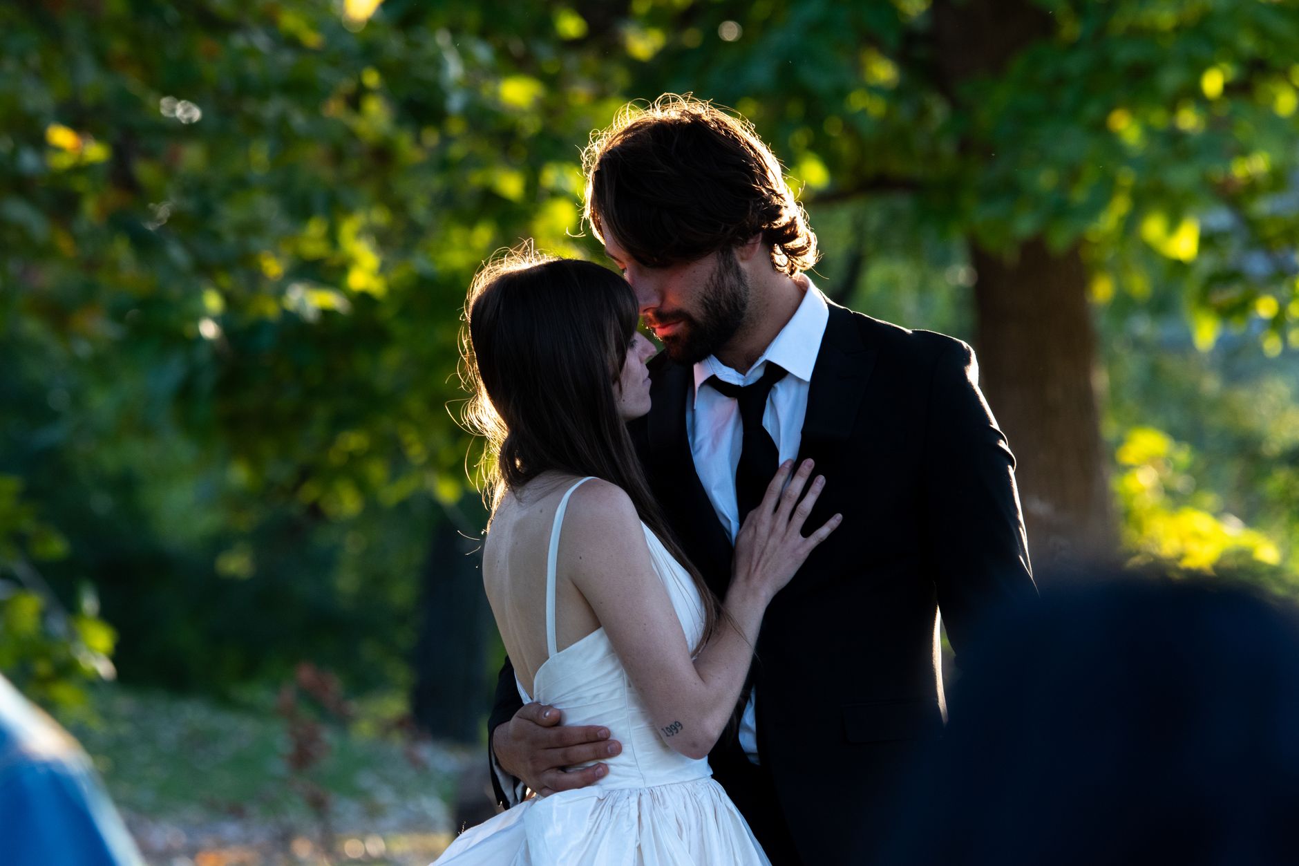 Young couple embracing in a tender moment outdoors with sunlight filtering through trees.