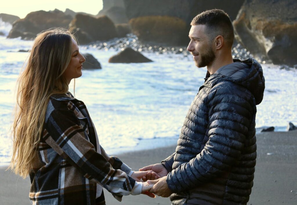 A couple holding hands on Vik Beach, Iceland, sharing an intimate moment by the rocky coast.