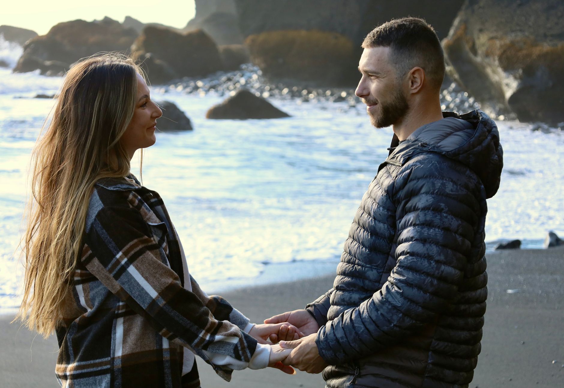 A couple holding hands on Vik Beach, Iceland, sharing an intimate moment by the rocky coast.