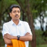 Portrait of a confident man with arms crossed, standing outdoors in a natural setting.