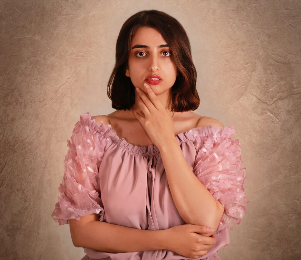 A beautiful woman poses confidently in a pink dress against a textured background.