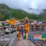 Vibrant view of Badrinath Temple surrounded by lush mountains and visitors crossing a bridge.
