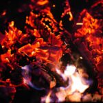 An intense close-up of glowing hot coals and vibrant flames at night, creating a fiery spectacle.