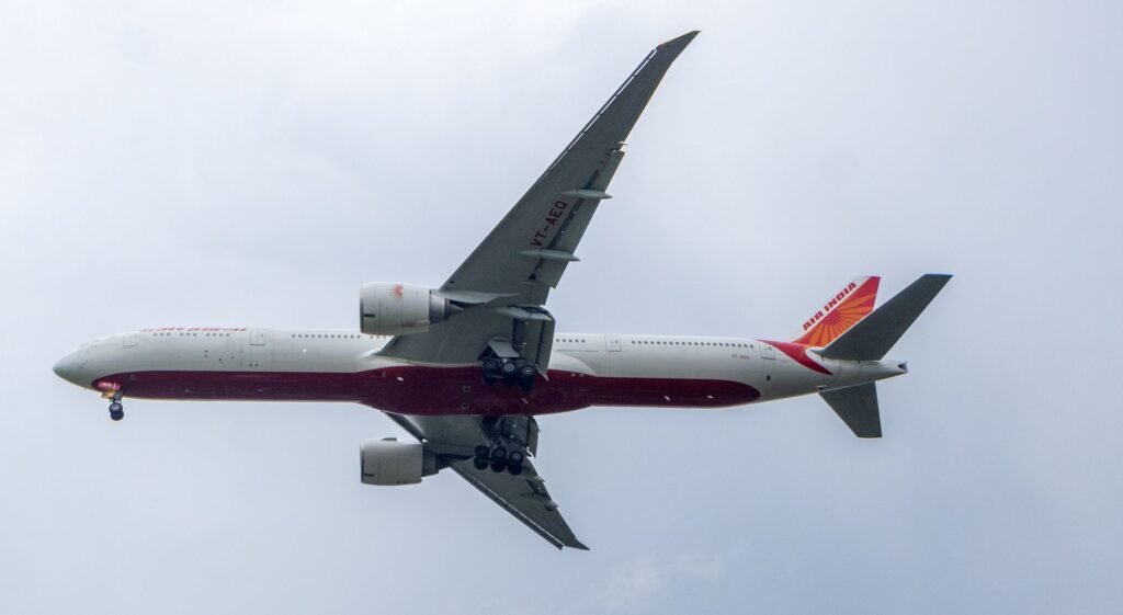 Close-up of an airplane mid-air with landing gear visible against a cloudy sky backdrop.
