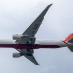 Close-up of an airplane mid-air with landing gear visible against a cloudy sky backdrop.
