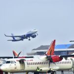 Airplanes on tarmac with one taking off at a busy airport on a clear day.