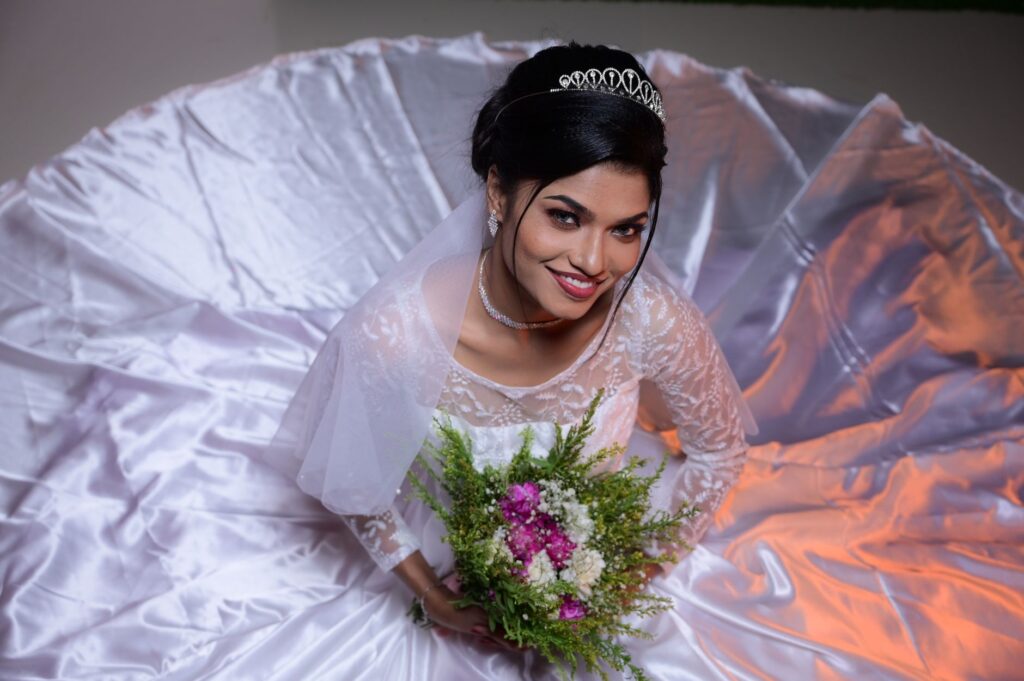 A beautiful bride in a satin dress holds a bouquet, smiling warmly. Photographed from above.