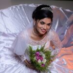 A beautiful bride in a satin dress holds a bouquet, smiling warmly. Photographed from above.