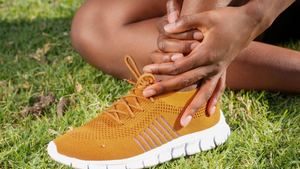 Close-up of athlete holding ankle with running shoe on grass, indicating pain or injury.