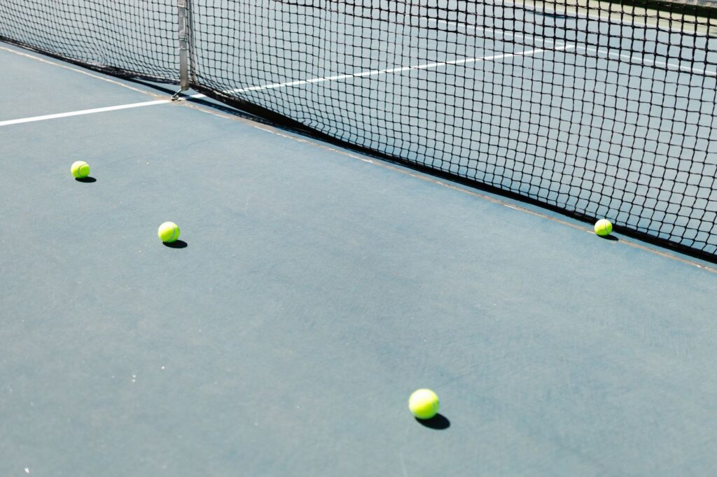 A tennis court featuring a net and several tennis balls lying on the ground, well-lit by sunlight.