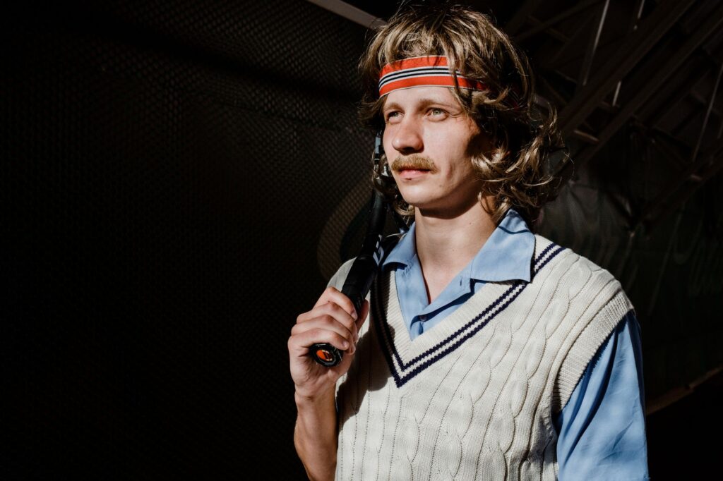 Portrait of a retro-styled tennis player with a racquet and headband, evoking a 70s vibe.
