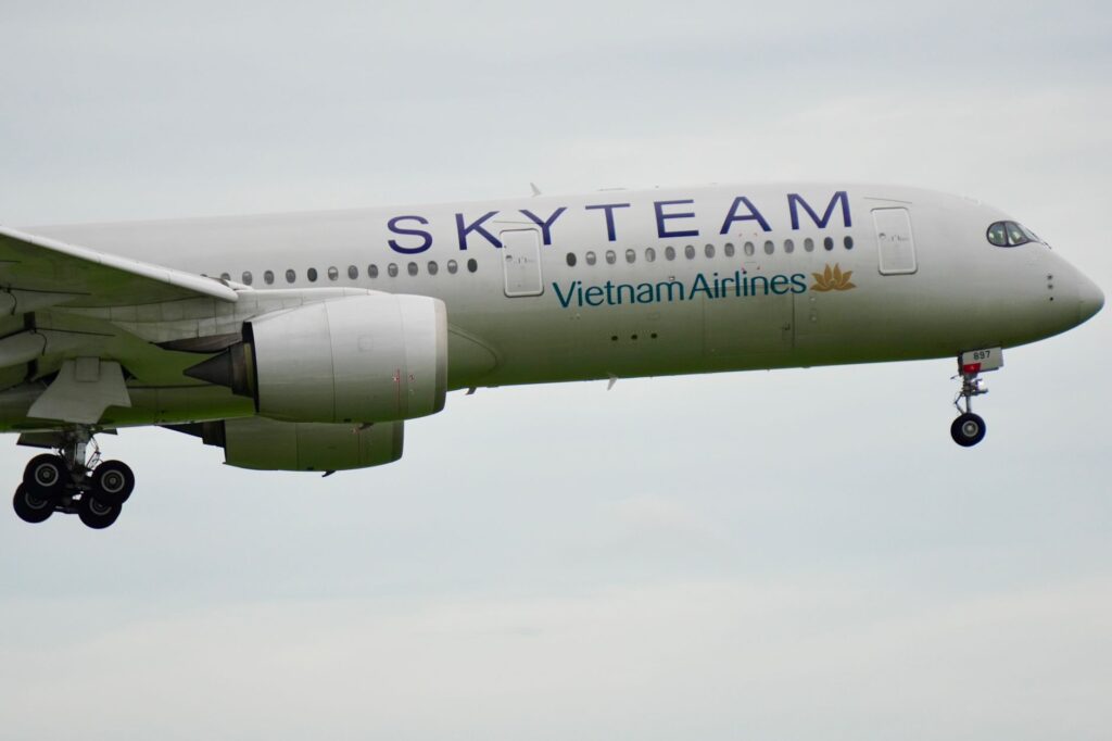 A Vietnam Airlines plane in SkyTeam livery flying in clear sky, showcasing its underbelly and landing gear.