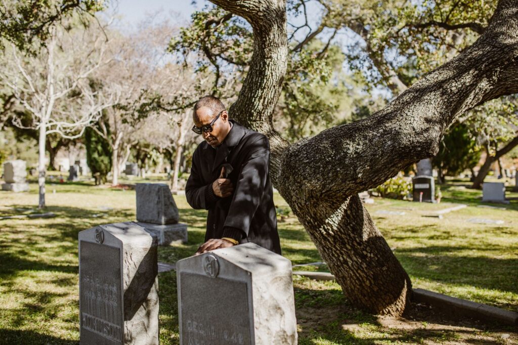 Elderly man grieving at a cemetery beside a tombstone, reflecting mourning and remembrance.