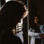 Two women facing a tense emotional exchange in a dimly lit room.
