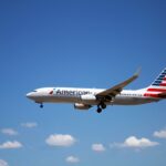An American Airlines plane flying through a clear blue sky, showcasing aviation travel.