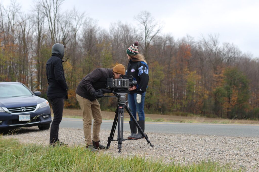Film crew capturing outdoor scenes with camera and tripod in autumn near Stratford, Ontario.