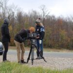 Film crew capturing outdoor scenes with camera and tripod in autumn near Stratford, Ontario.