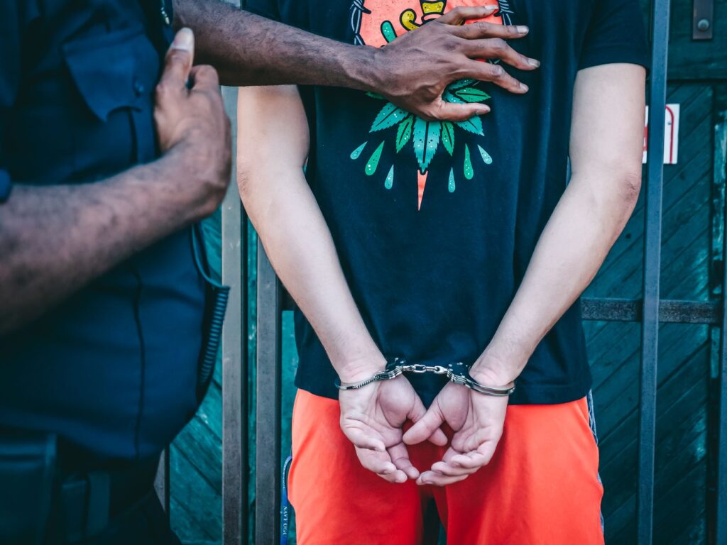 Close-up of a handcuffed person under arrest by a police officer outdoors.