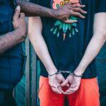 Close-up of a handcuffed person under arrest by a police officer outdoors.