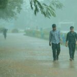 Two men stroll through a park pathway during a heavy rain shower, enjoying the rainy day.