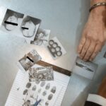 Hands of a handcuffed man examining criminal evidence with an officer.