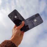 Close-up of a hand holding two smartphones against a cloudy sky, showcasing modern technology.