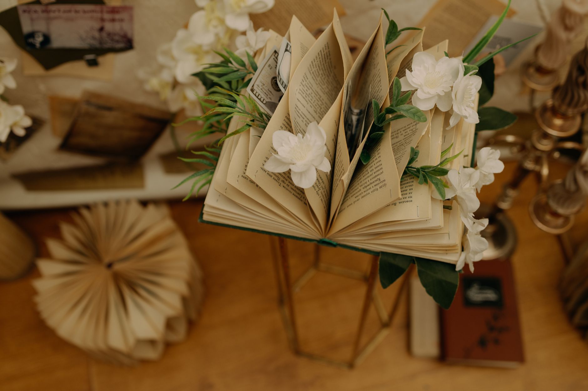An artistic composition featuring an open book adorned with white flowers, placed on a vintage stand.