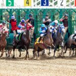 Dynamic scene of jockeys and horses launching from starting gate in a competitive race.