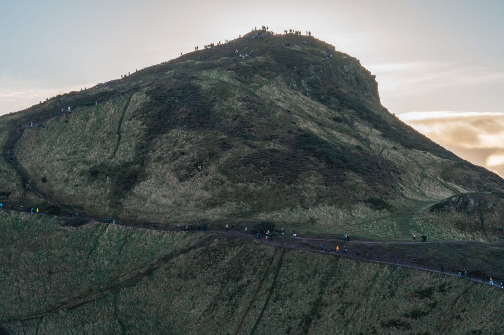 Scenic view of Arthur's Seat in Edinburgh with people hiking at sunset.