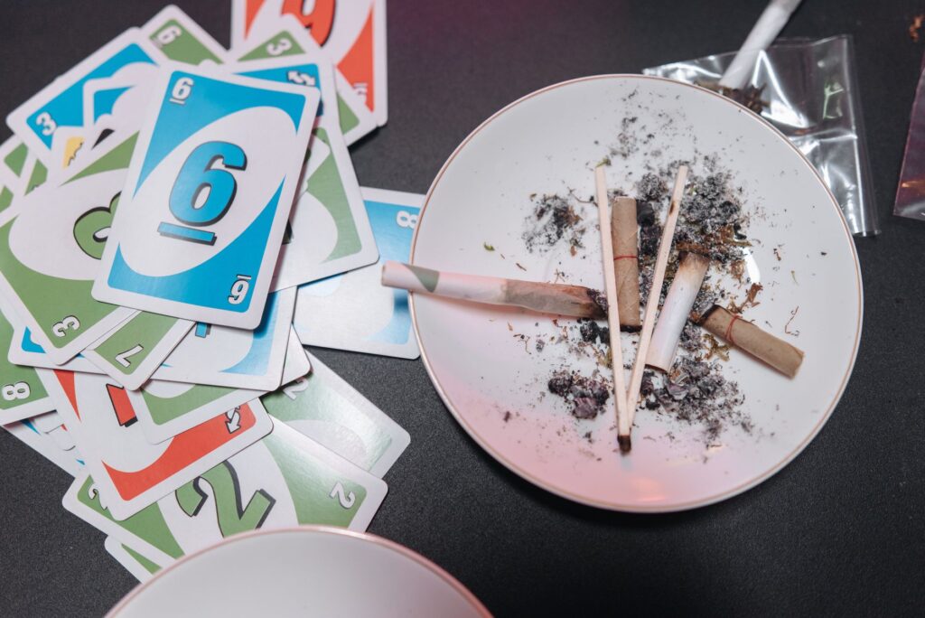Close-up of a plate with ashes and burnt joints surrounded by playing cards.