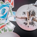 Close-up of a plate with ashes and burnt joints surrounded by playing cards.