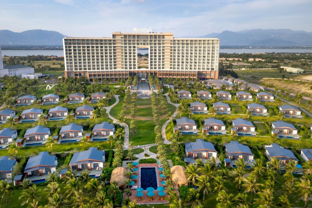 Aerial view of a luxury resort with bungalows surrounded by mountains and palm trees.