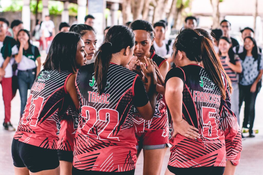 An Asian women's volleyball team in a huddle, preparing for a competitive match indoors.