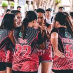 An Asian women's volleyball team in a huddle, preparing for a competitive match indoors.