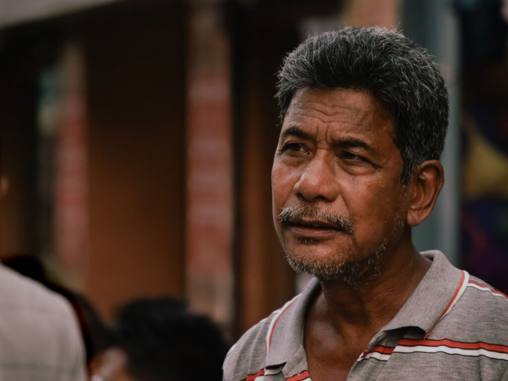 Candid portrait of a thoughtful senior man with facial hair wearing a polo shirt in Guwahati, India.