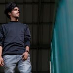 Portrait of a young South Asian man in black sweater with a confident expression.