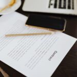 Close-up of a contract with office essentials like a laptop and coffee on a desk.