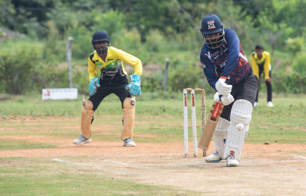 Cricket batsman facing bowler with wicketkeeper and fielder outdoors.