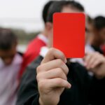 Referee showing a red card to players during an outdoor soccer game.