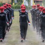 Group of Paskibra members marching in formation outdoors wearing uniforms and red caps.