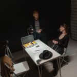A tense indoor interrogation scene depicting a suspect and law enforcement setup.