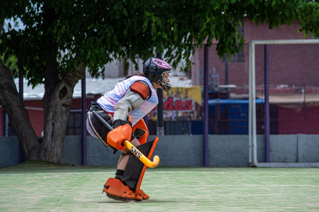 A field hockey goalie in protective gear, ready for action on an outdoor field.